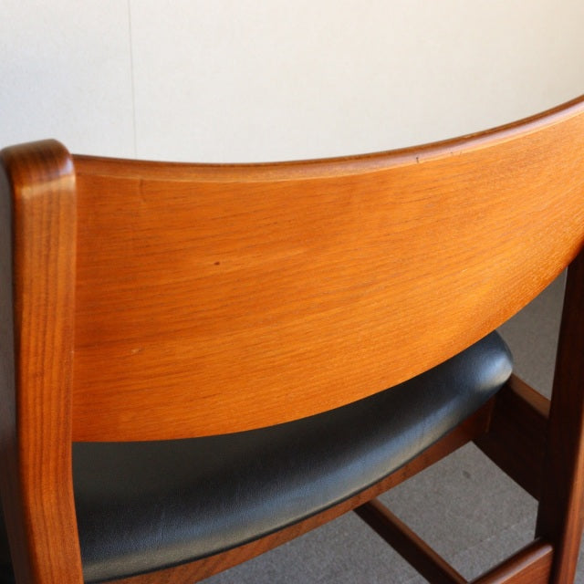 Mid-century British vintage dining chair with smooth teak wood grain and black leather seat.