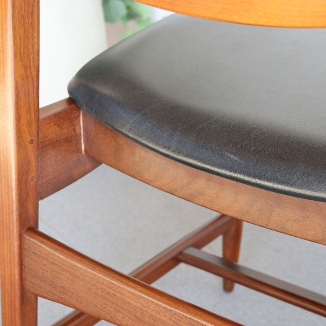 Vintage British mid-century teak dining chair with black leather cushioned seat and visible wood grain.