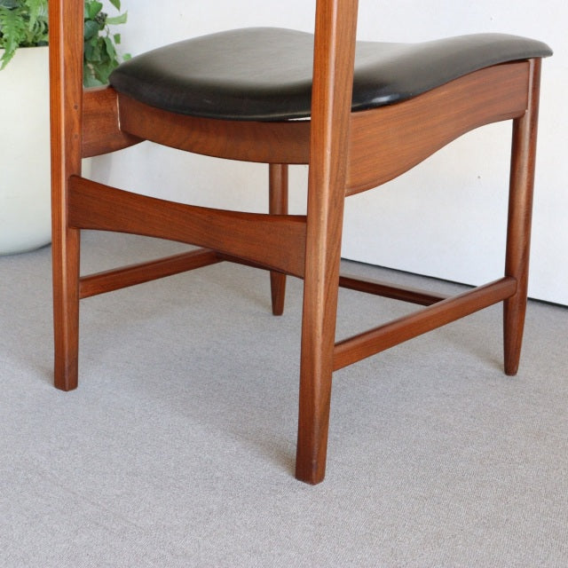 Mid-century British vintage dining chair with warm teak wood frame and curved black leather seat cushion, showcasing fine.