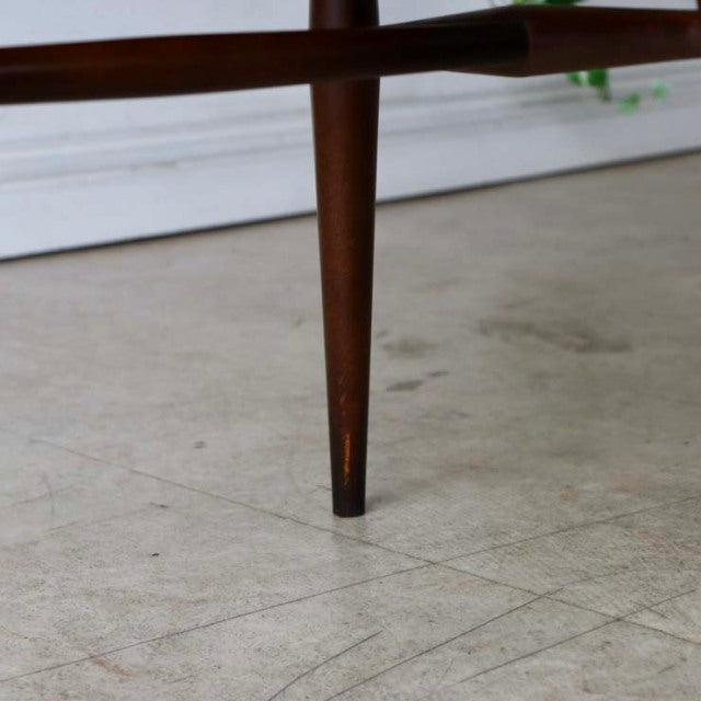 Mid-century British vintage teak dining chair leg with slender tapered wood grain and brass-capped tip on light floor.