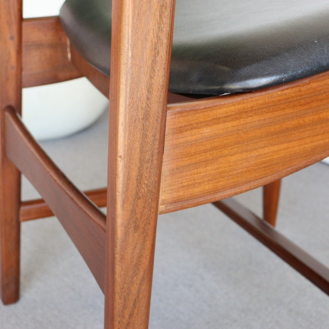 Mid-century British vintage dining chair with rich teak wood grain, black leather seat, and sturdy wooden legs from Denmark.