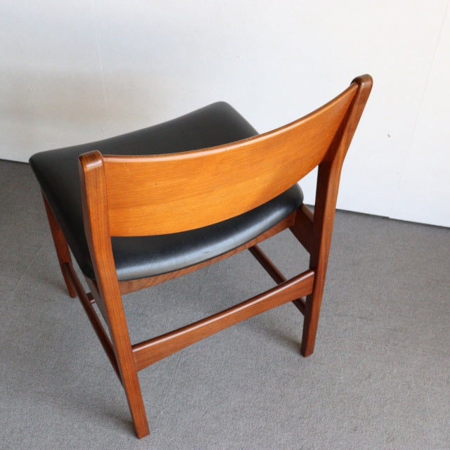 Vintage British mid-century dining chair in teak wood with smooth grain, black leather seat, and tapered legs.
