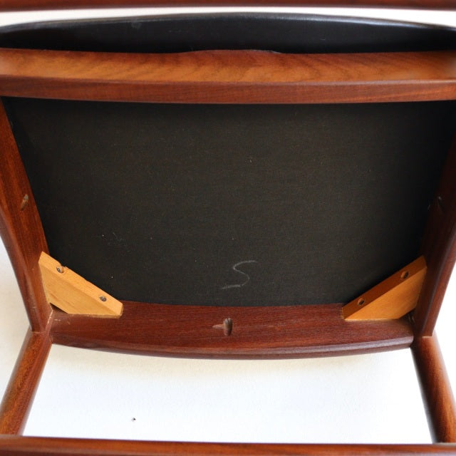 Vintage British mid-century dining chair underside showing solid teak frame, black leather seat, and sturdy wood grain legs.