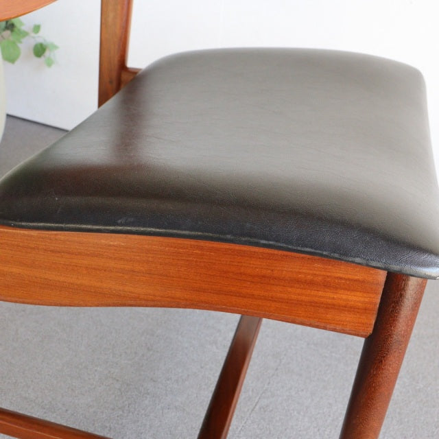 Mid-century British vintage dining chair with rich teak wood frame and smooth black leather seat cushion.