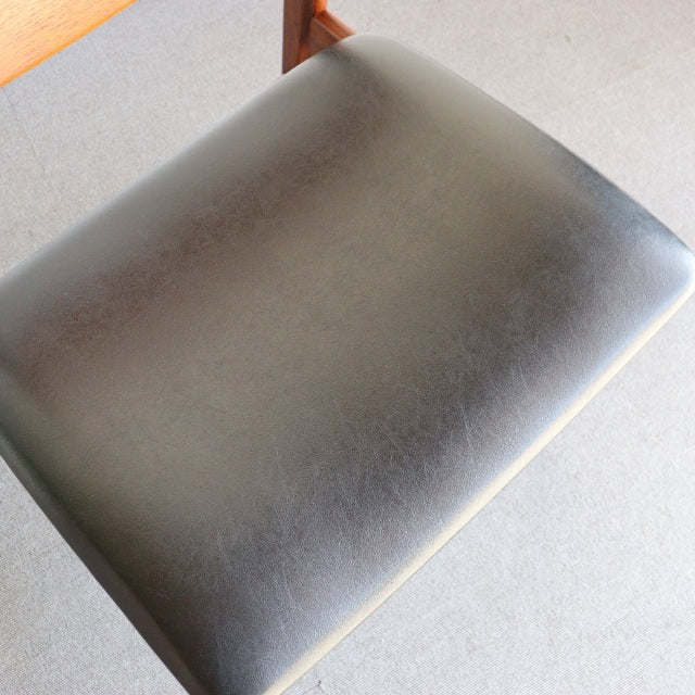 Mid-century vintage British dining chair with black leather seat cushion and teak wood frame showing natural grain.