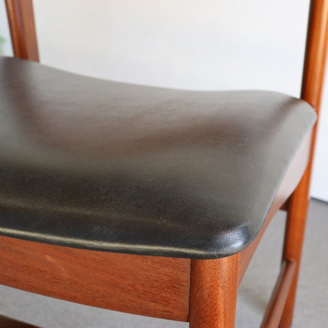 Vintage British mid-century dining chair with smooth black leather seat and warm teak wood frame showcasing natural grain.
