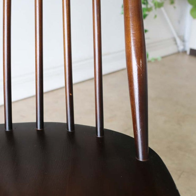 Close-up of vintage British mid-century Ercol Goldsmith dining chair with teak spindle back and rounded dark wood seat.