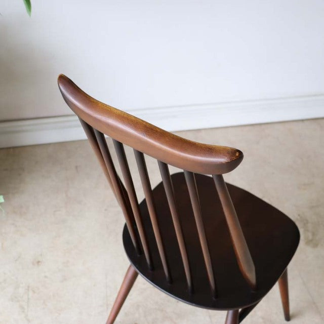Vintage British mid-century teak dining chair by Ercol with curved spindle back and tapered legs, showcasing rich wood grain .
