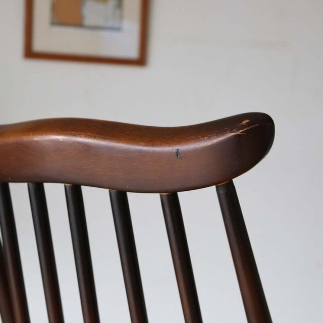 Mid-century British vintage teak dining chair with curved armrest and slender spindle backrest, smooth wood grain finish.