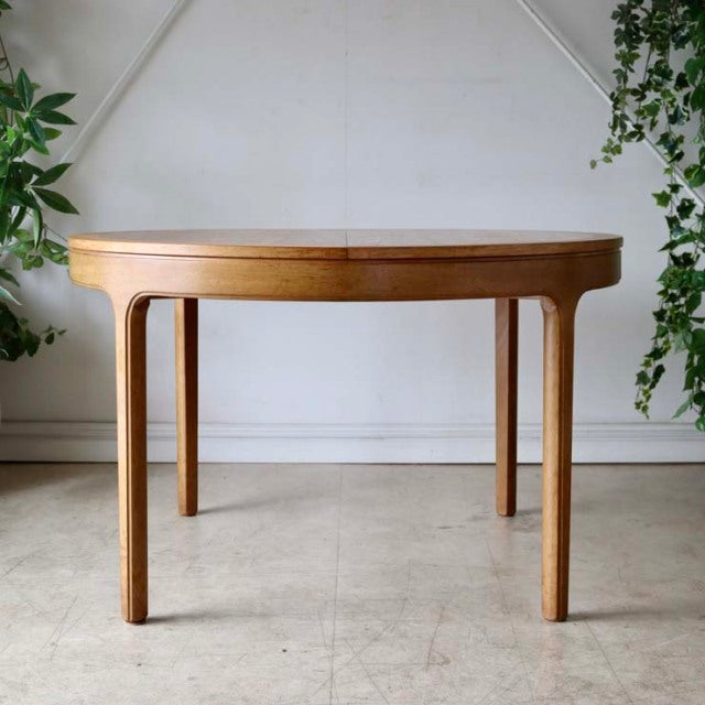 Mid-century vintage British teak round dining table by Nathan with smooth wood grain and tapered legs.