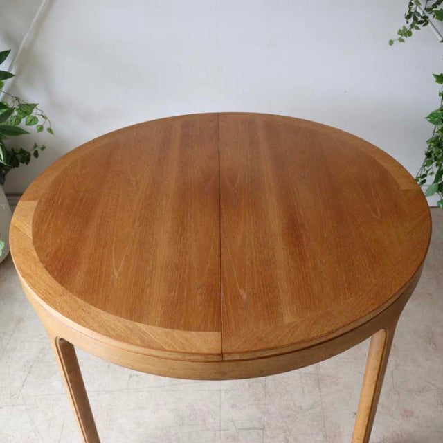 Vintage Nathan round teak dining table with smooth wood grain, slender tapered legs, British mid-century design inspired by.