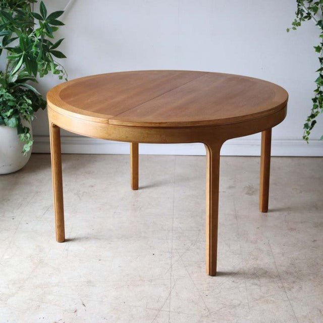 Round vintage teak dining table by Nathan with smooth wood grain, slender legs, mid-century British design inspired by.