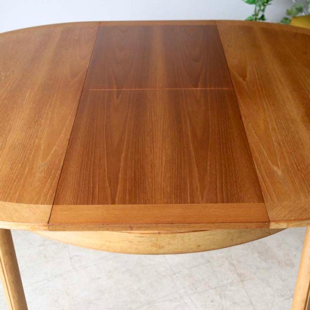 Vintage British mid-century teak round dining table with rich wood grain and slender tapered legs from Denmark.
