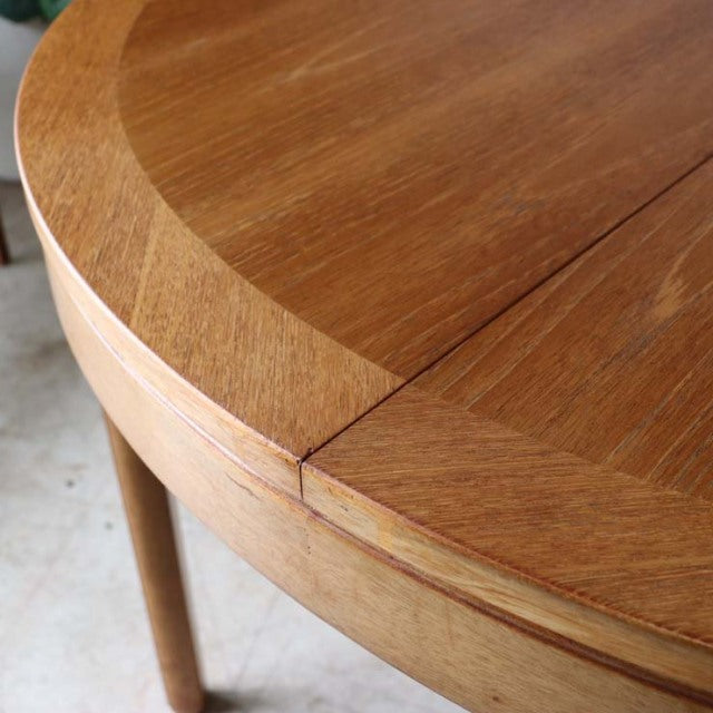 Vintage teak round dining table with visible wood grain, British mid-century design from Denmark, sleek tapered legs.