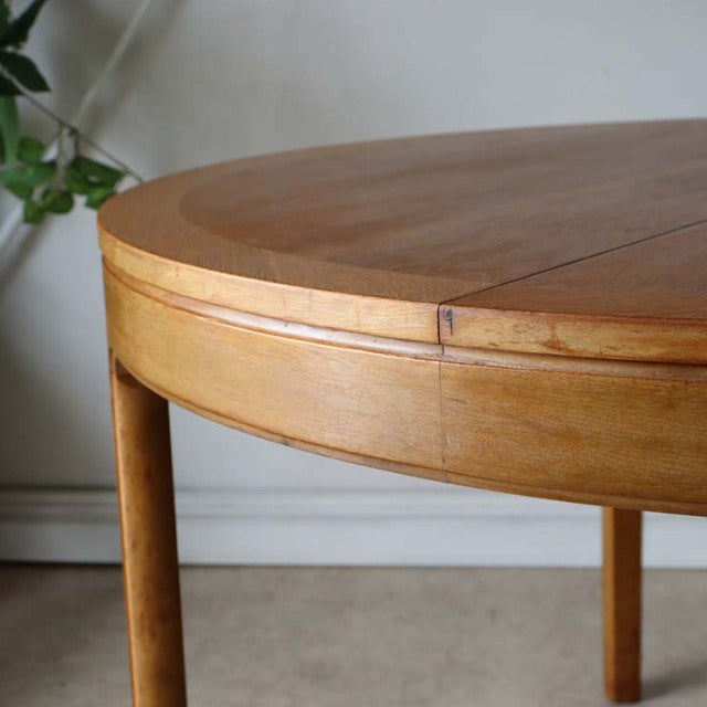 Vintage mid-century teak round dining table with smooth wood grain and slender cylindrical legs, British-Denmark design.