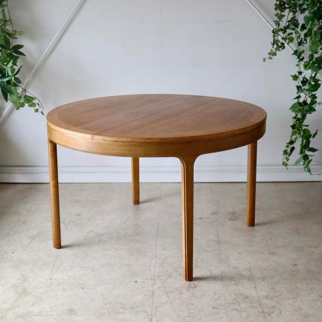 Round vintage teak Nathan dining table with slender tapered legs, mid-century British-Denmark design, smooth wood grain.