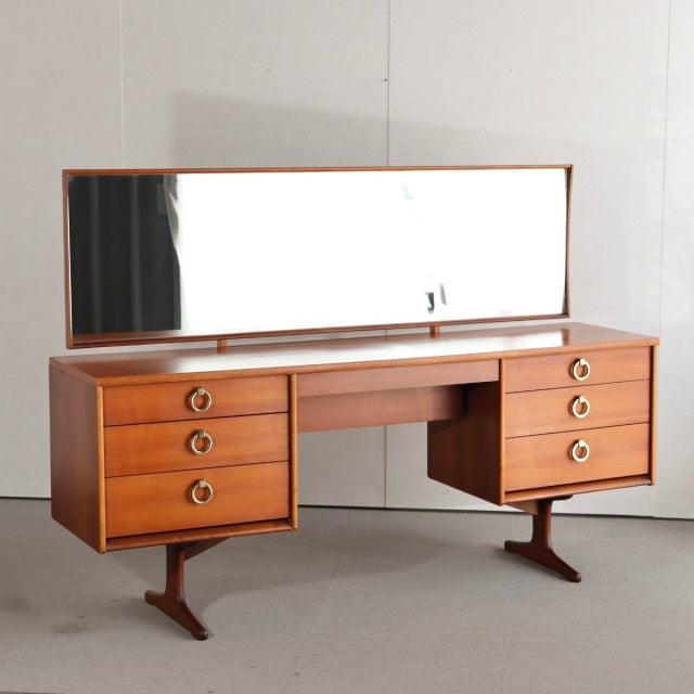 Mid-century British vintage teak dresser with six drawers, round brass handles, long rectangular mirror, and tapered legs.