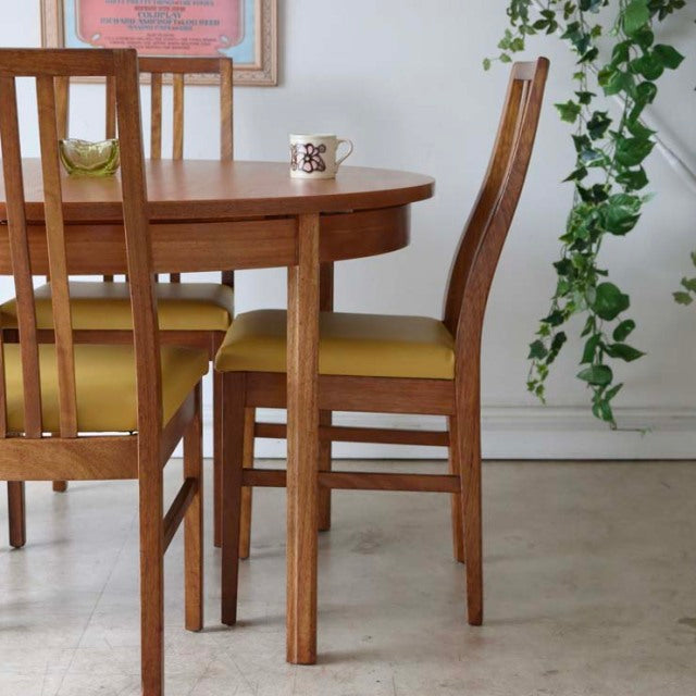 Vintage mid-century Alfred Cox teak round dining table with slender tapered legs and smooth wood grain, paired with matching .