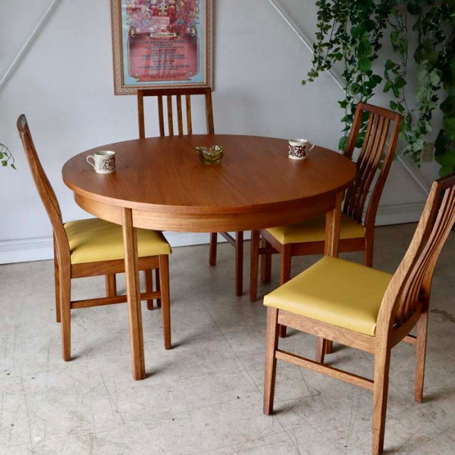 Vintage Alfred Cox mid-century round teak dining table with tapered legs and four matching chairs featuring vertical slat.