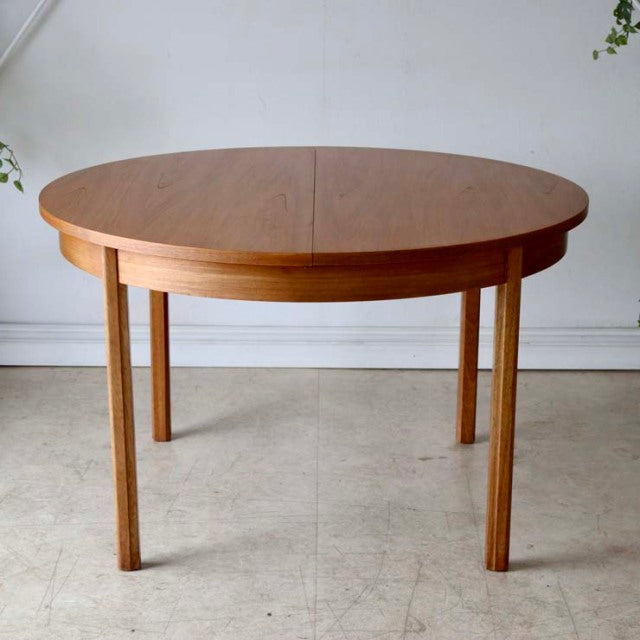 Vintage Alfred Cox round teak dining table with British mid-century design, clean wood grain, slender straight legs, and.