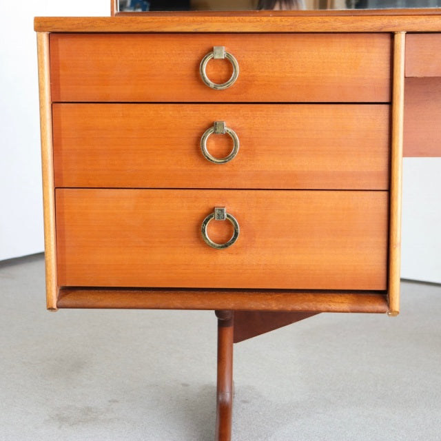 Mid-century British vintage teak dresser drawers with brass ring handles and visible wood grain on slender legs.