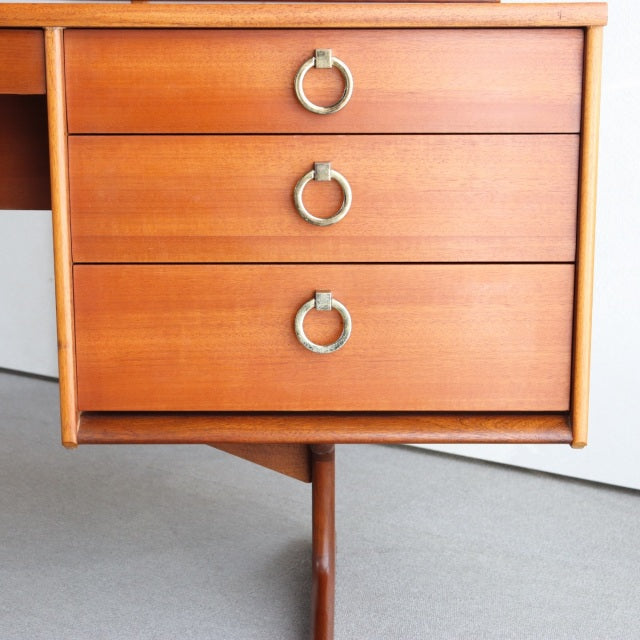 Mid-century British vintage teak dresser with three drawers, circular metal ring pulls, tapered legs, and visible wood grain.