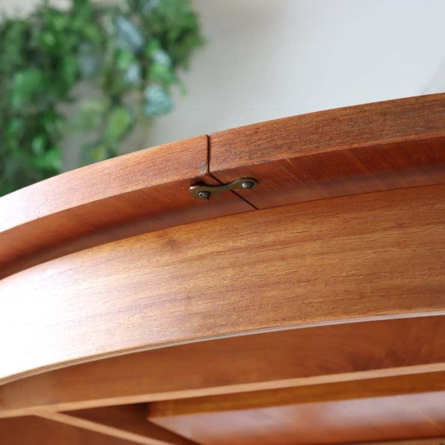 Close-up of vintage British mid-century Alfred Cox teak round dining table edge showing rich wood grain and brass hinge.