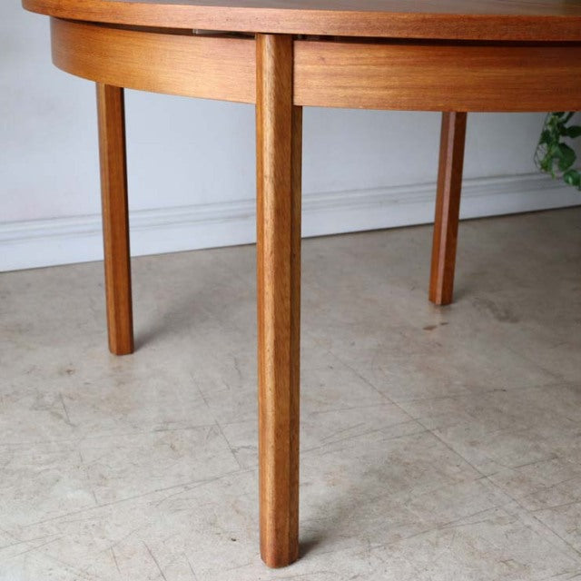 Vintage Alfred Cox round teak dining table with smooth wood grain and tapered mid-century British legs.