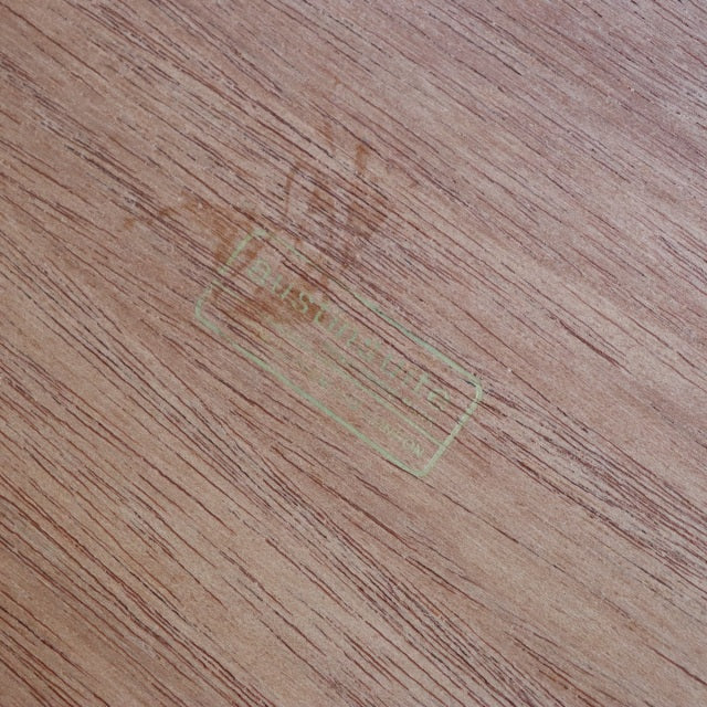 Close-up of vintage teak wood grain with faded gold AUSTINSUITE British mid-century Denmark maker's mark on smooth surface.