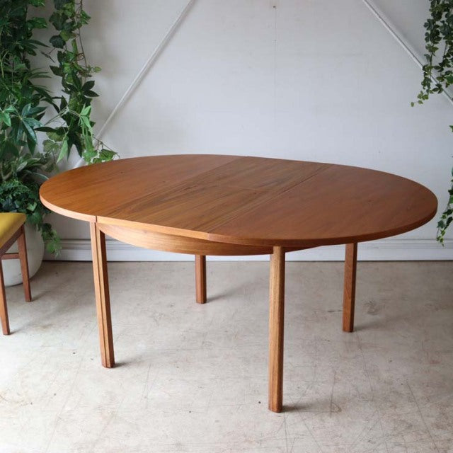 Vintage mid-century British Alfred Cox round dining table in teak with smooth wood grain and slender tapered legs from.