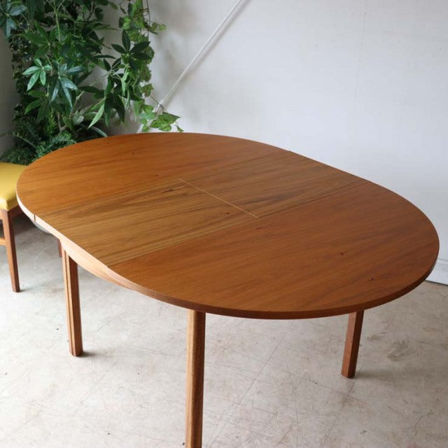 Vintage mid-century British Alfred Cox round teak dining table with smooth wood grain and slender tapered legs.