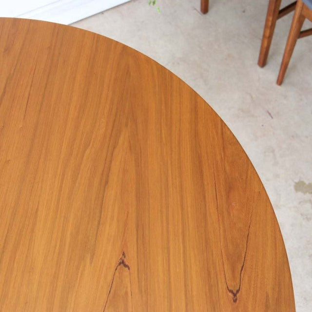 Round vintage teak dining table with smooth wood grain, mid-century British design by Alfred Cox, Denmark style legs visible .