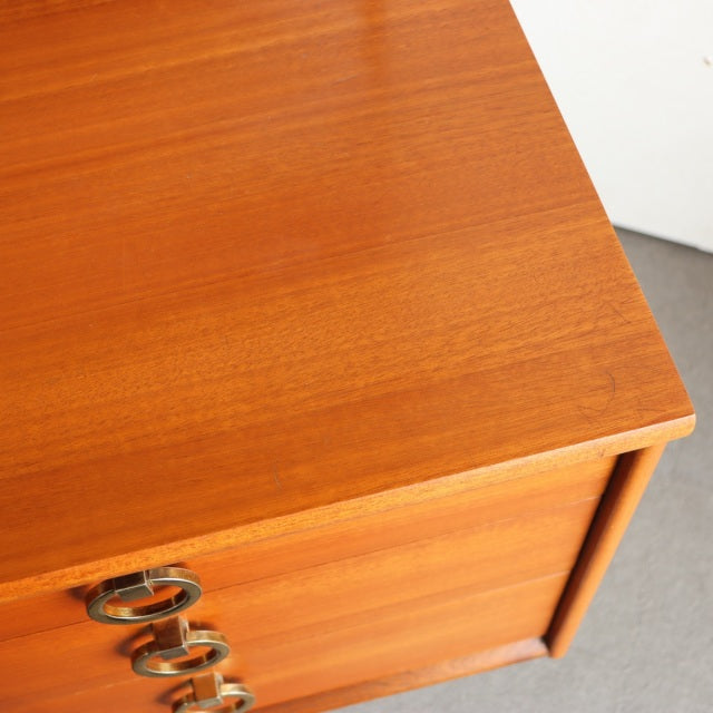 Vintage teak mid-century dresser corner with smooth wood grain and brass ring drawer pulls, British-Denmark style.