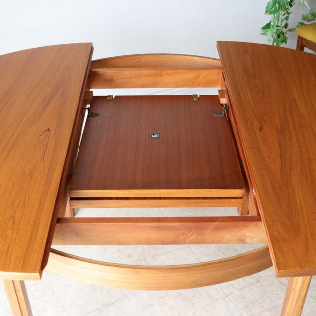 Vintage Alfred Cox mid-century teak dining table with round top, extending mechanism, and sturdy wooden legs in.