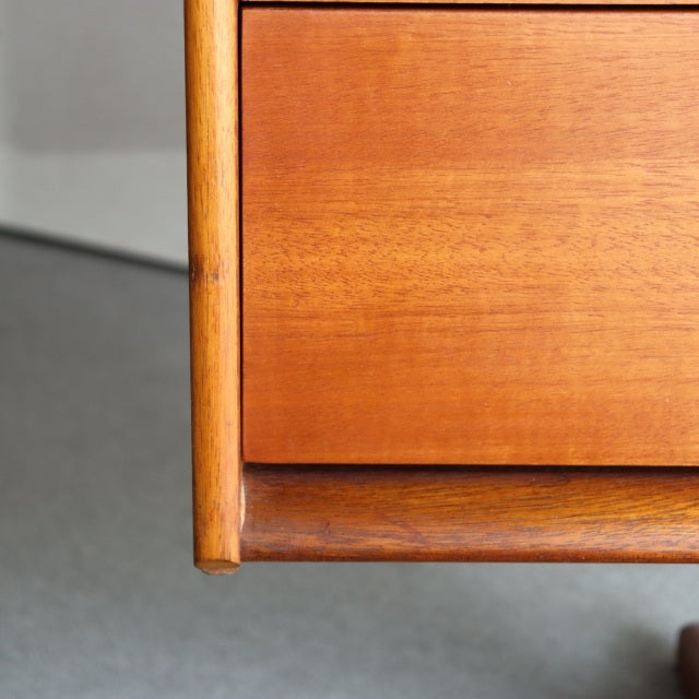 Close-up of vintage teak dresser corner showing smooth wood grain and rounded British mid-century design details.