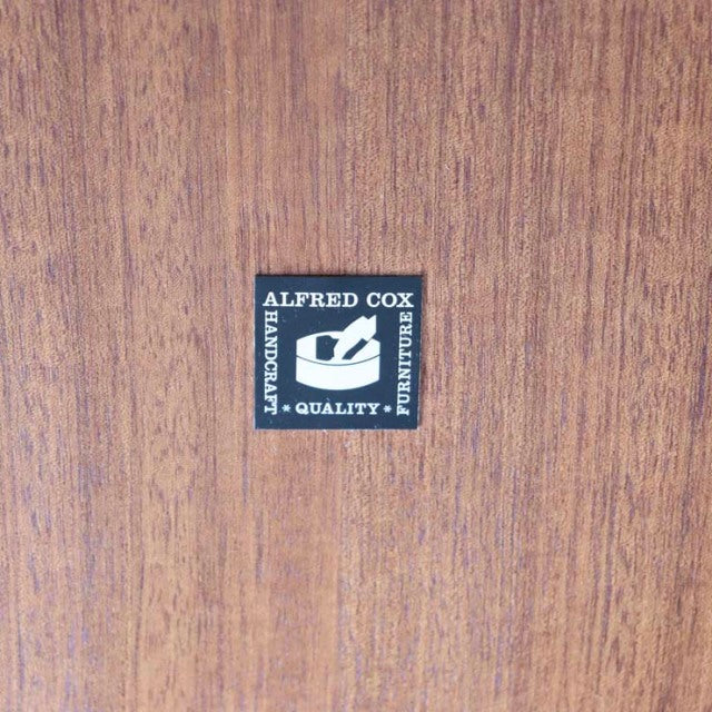Close-up of Alfred Cox vintage British teak dining table with rich wood grain and branded label centered on the surface.