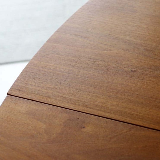 Vintage Alfred Cox teak round mid-century dining table from Britain with smooth wood grain and elegant curved edge.