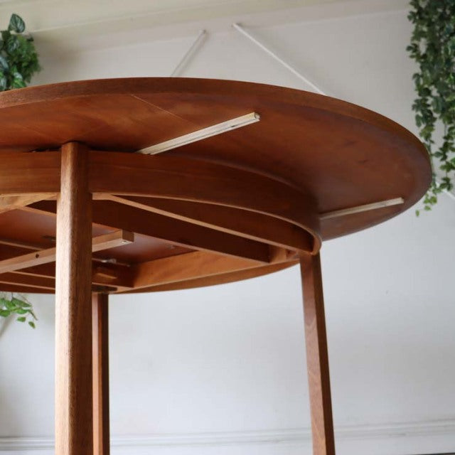 Vintage British mid-century Alfred Cox round teak dining table with smooth wood grain and tapered legs viewed from below.