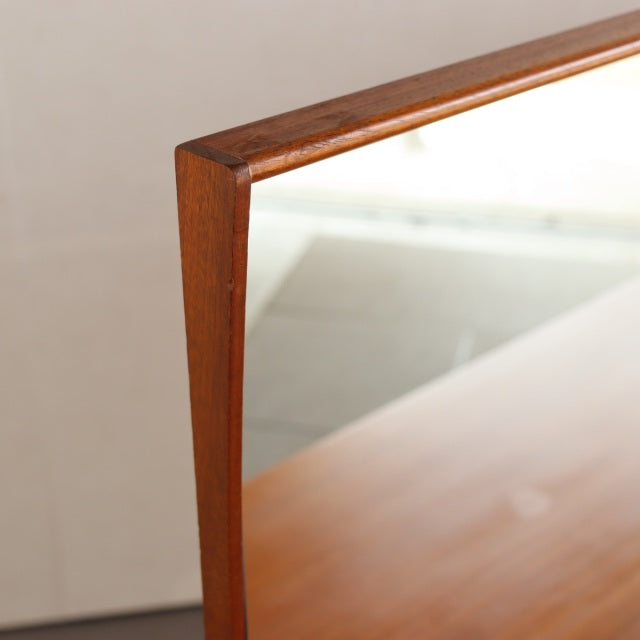 Close-up of vintage mid-century British teak dresser mirror corner with smooth wood grain and sharp angled frame.