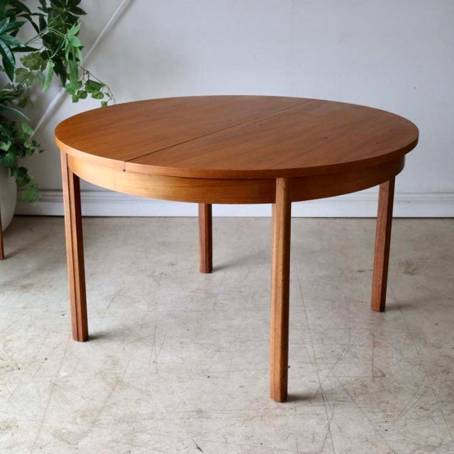 Vintage British mid-century round dining table in teak with smooth wood grain and slender tapered legs from Alfred Cox.