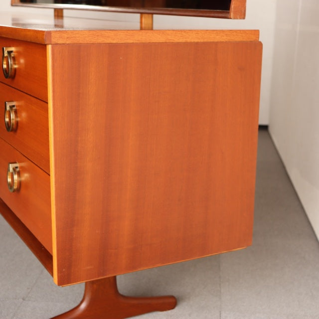 Mid-century British vintage teak dresser side view showing smooth grain and rounded edges with slender tapered leg.