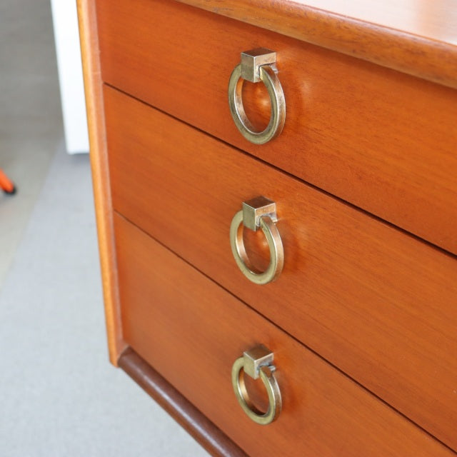 Vintage mid-century British teak dresser with three drawers, brass ring pulls, and smooth wood grain finish.