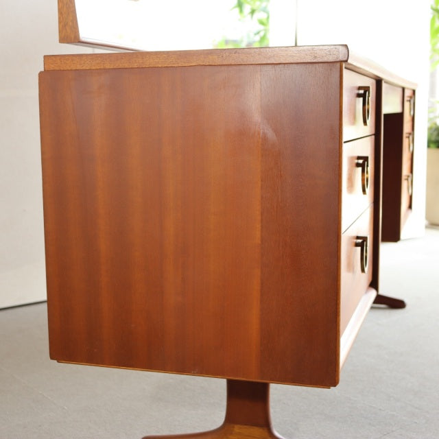 Mid-century British teak dresser with sleek wood grain, smooth side panel, and sturdy tapered legs.