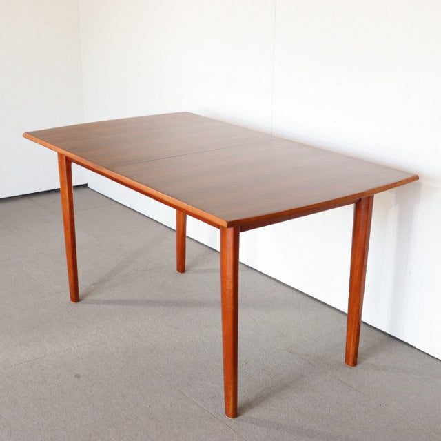 Mid-century British teak dining table with rectangular top, fine wood grain, and slender tapered legs.