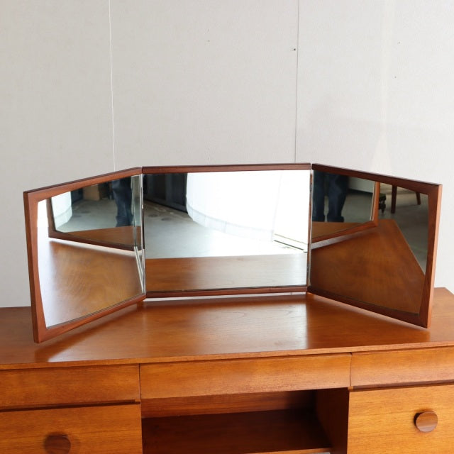 Vintage mid-century British teak dresser with three-panel adjustable mirrors and visible wood grain on smooth surface.