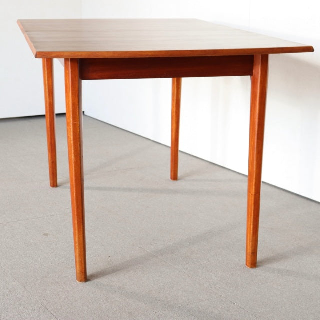 Vintage mid-century British teak dining table with rectangular top and slender tapered legs, smooth wood grain finish from.