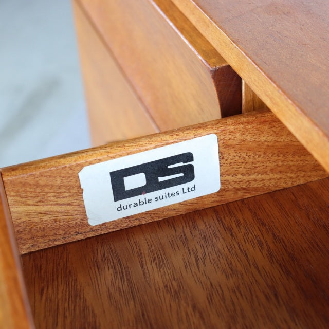 Close-up of vintage teak dresser drawer corner showing warm wood grain and Durable Suites Ltd label inside, reflecting.