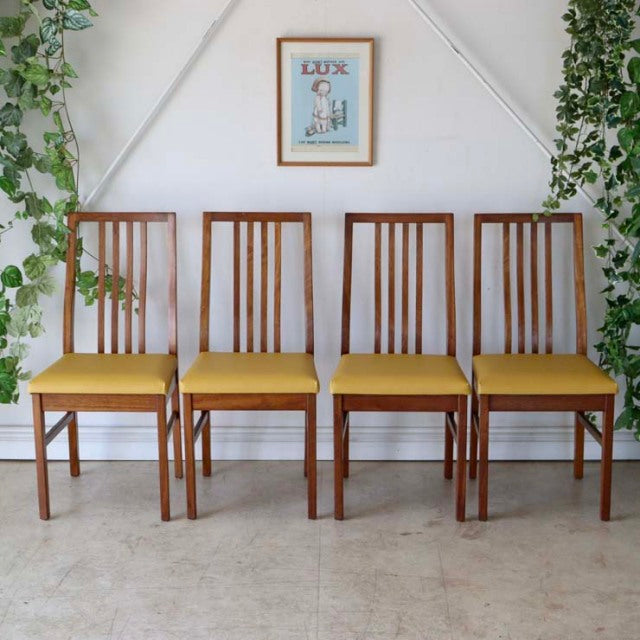 Set of four vintage teak dining chairs with yellow upholstered seats, sleek British mid-century design, straight legs, and.