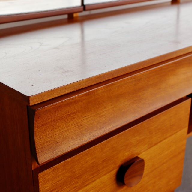 Vintage mid-century teak dresser with smooth wood grain, rounded drawer fronts, and a large circular knob, showcasing.