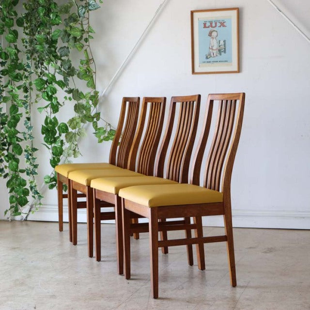 Set of four mid-century British vintage teak dining chairs with mustard yellow upholstered seats, tall slatted backs, and.